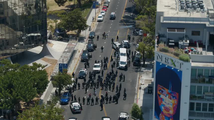 A mass of police officers surround a pair of protesters in a city street during the day