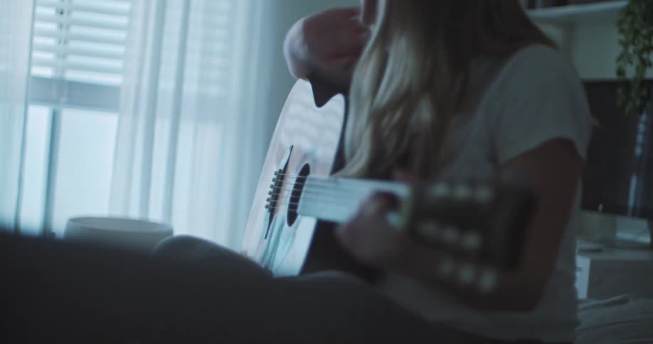 Female musician sits on bed playing guitar