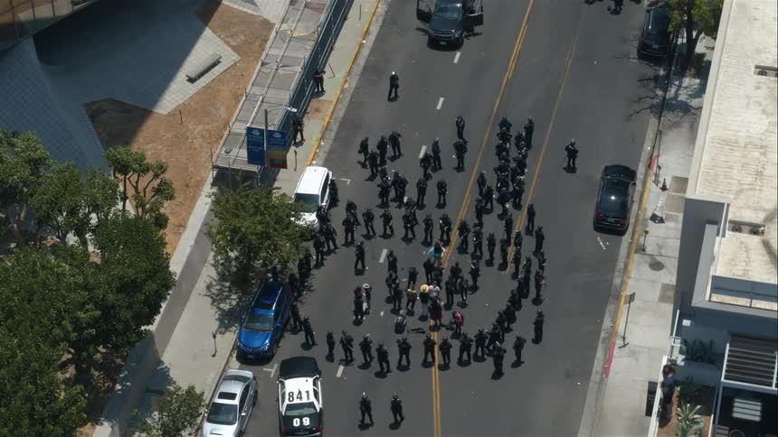Dozens of police officers surround suspects in a circle in a city street