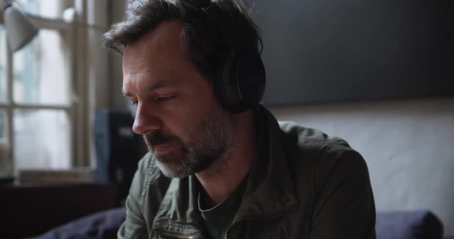A man in a room with headphones with a wall and window in the background