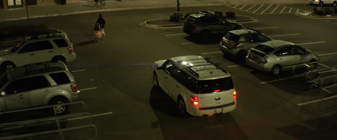 An suv travels slowly down a lane in a supermarket parking lot at night