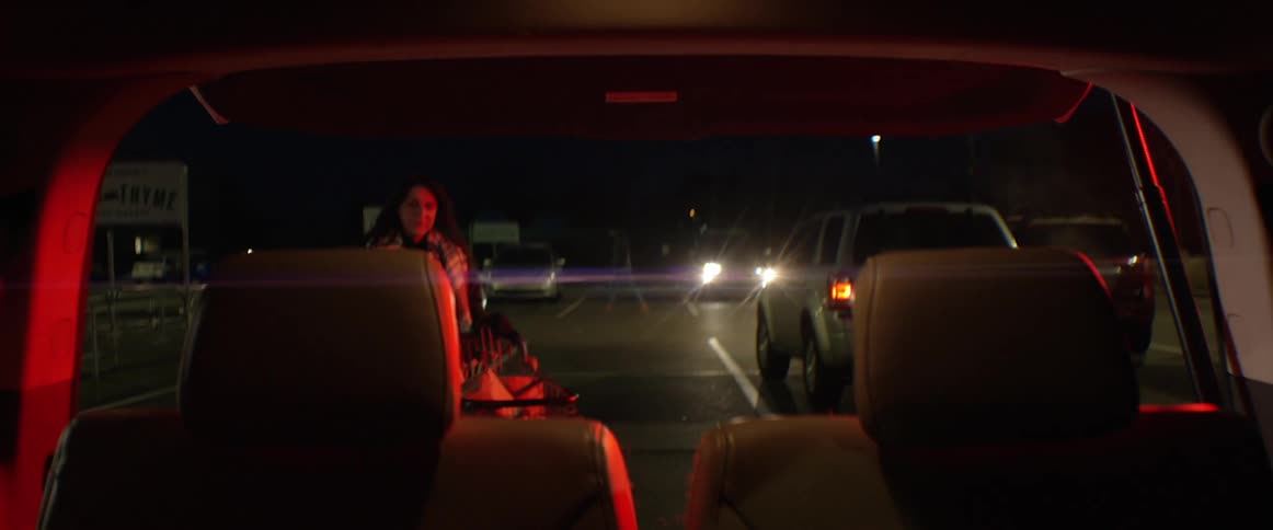 Woman unloads grocery cart into rear of vehicle at night
