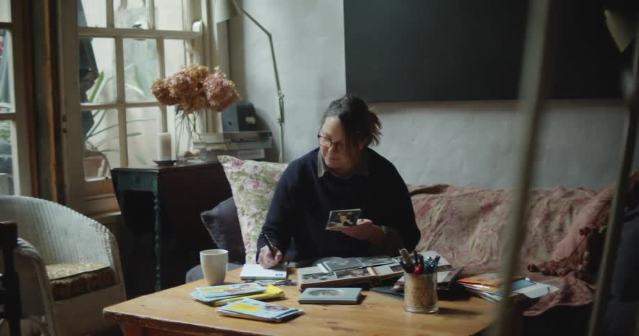 A woman sits on her couch at home and looks a photos and writes on a pad of paper