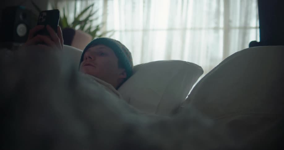 Man resting in bed at home checking his phone in the morning