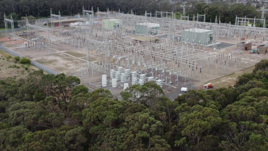 Electrical grid sits in the forest with a city in the distance