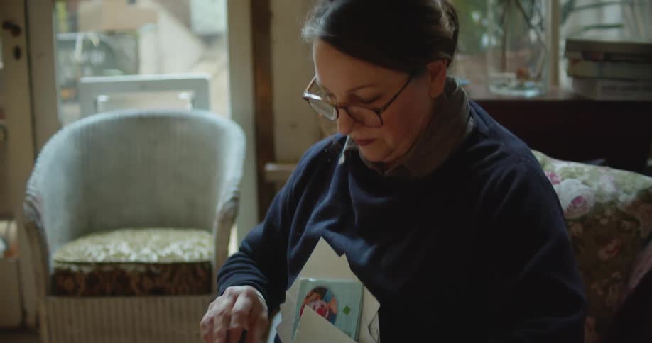 Woman sits on couch sorting through photographs