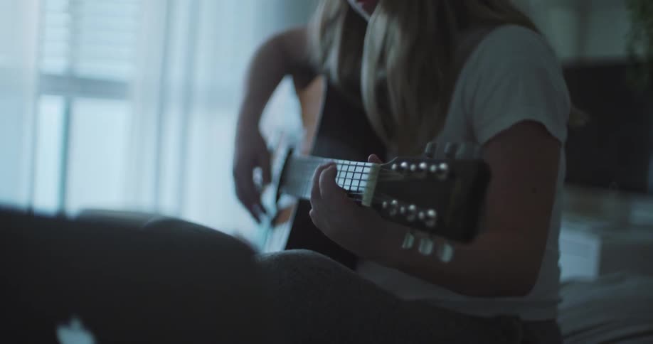 A woman sitting cross legged on a bed playing the guitar