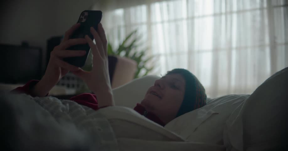 A man wearing a beanie cap lying in bed talking on his smart phone