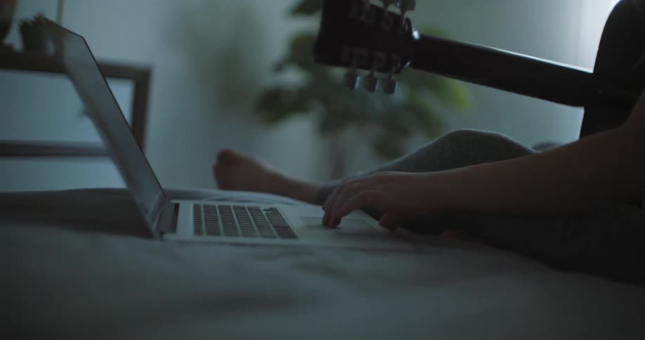 Musician holds guitar and manipulates nearby laptop with touchpad