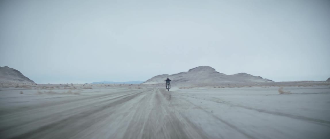A motocross rider speeds past sand dunes in the desert