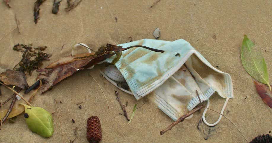 A dirty mask lies on the sand next to sticks and leaves