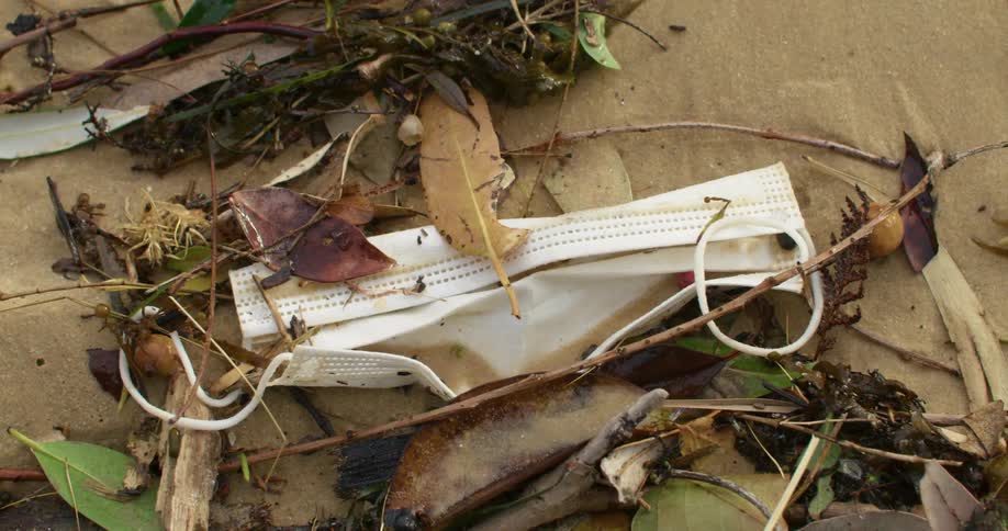 Dirty white face mask discarded over the sand surrounded by debris