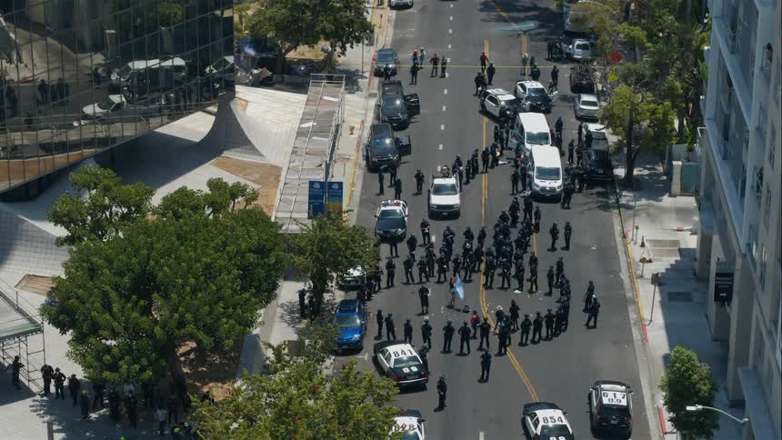 A protestor stands blocking the street waving a flag surrounded by police standing in a circle