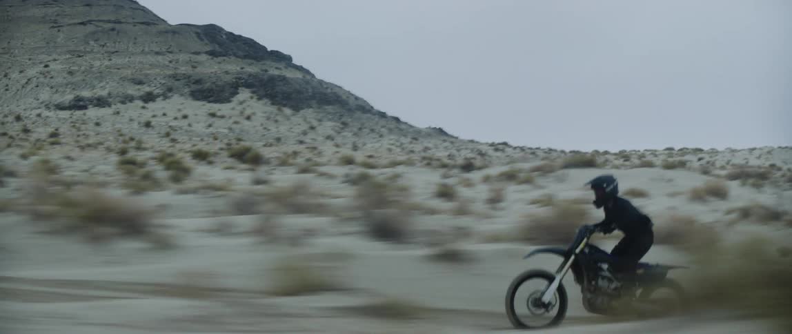 A person rides a dirt bike at a very high speed across a desert landscape