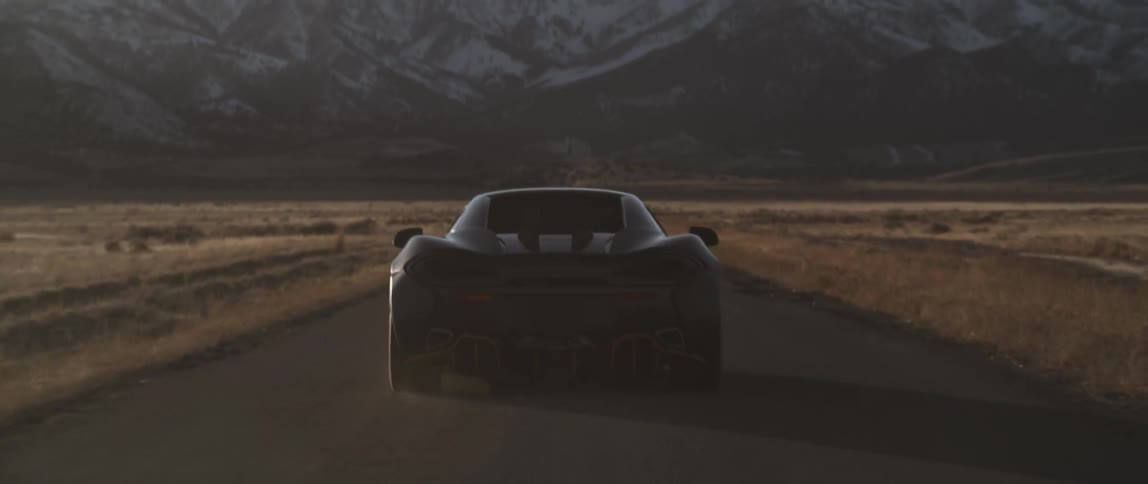 A sports car driving down a road near some mountains