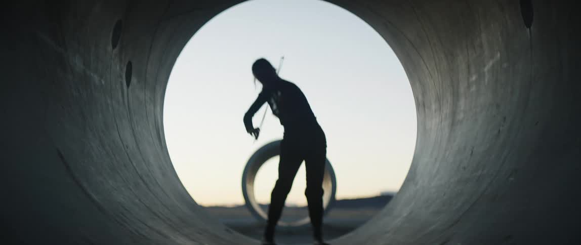 A silhouette of a woman inside a cylinder passionately playing a violin with the sky and clouds in the background