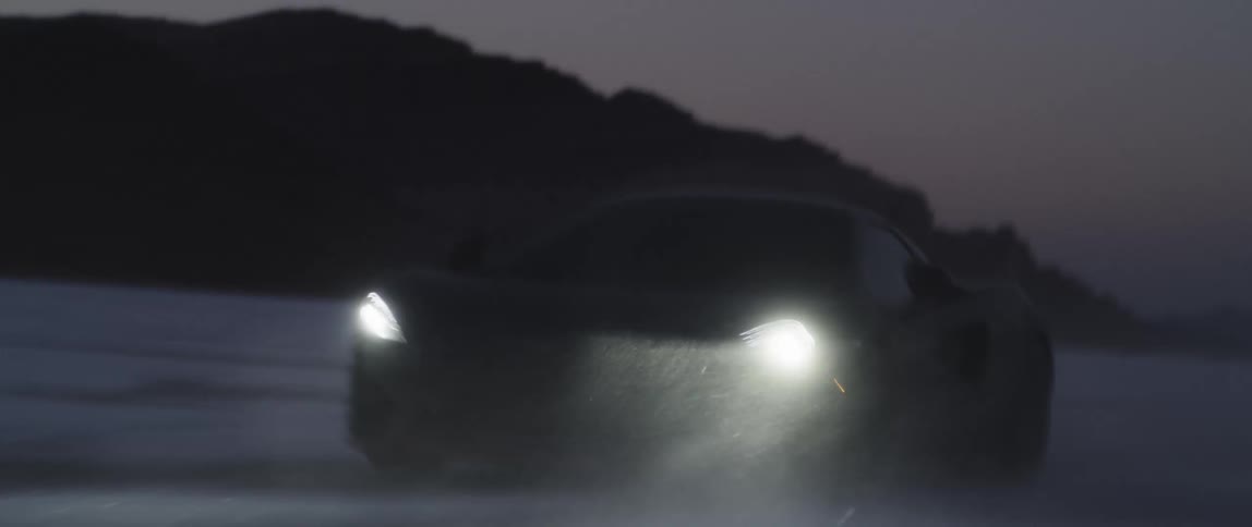 A sports car speeds along a snow dusted landscape in the dark of night