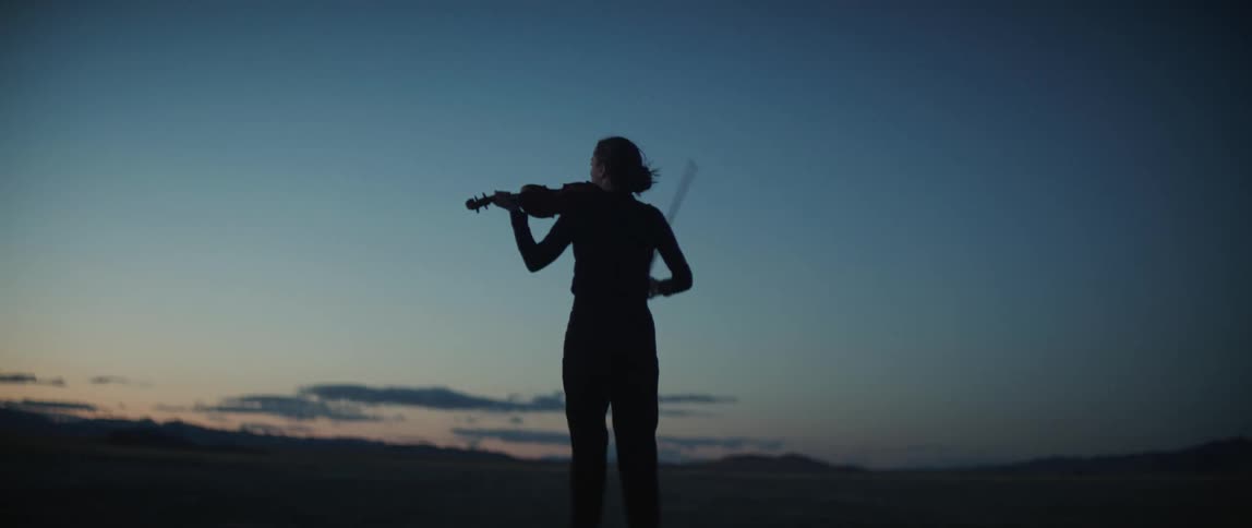 Woman stands in a field at night and begins to play a violin