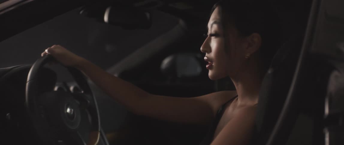 A woman sitting in the drivers seat of a sports car turns to look at the camera through the open door