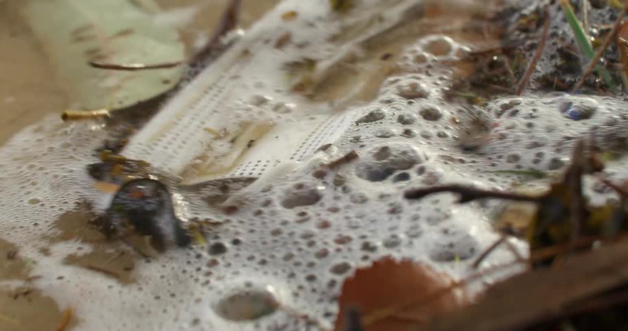 An ocean wave washes over a face mask and other debris discarded on the beach