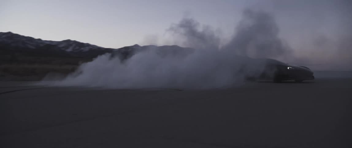 Black sports car smoking as it spins out while traveling on a road near snow covers hills