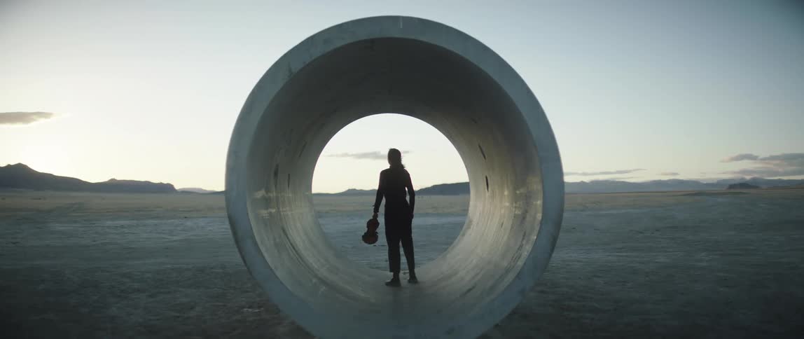 A woman finishes playing violin at sunset