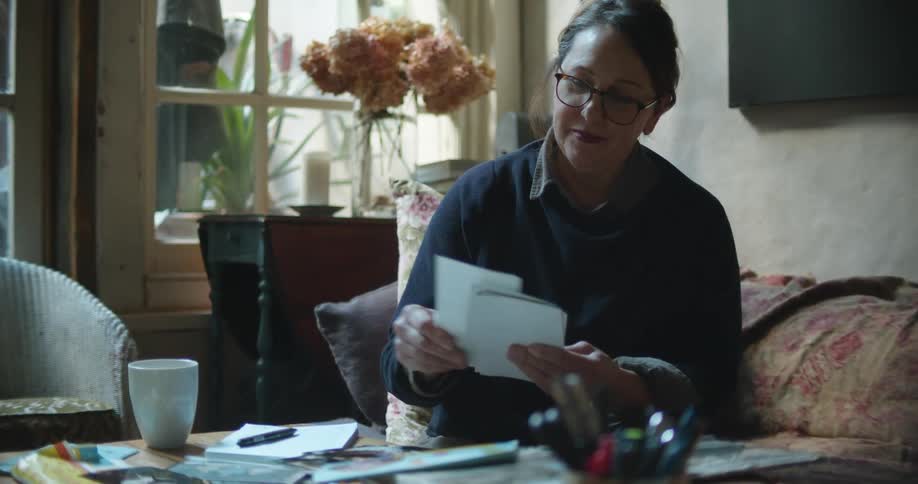A woman drinks coffee and smiles while going through a stack of photographs