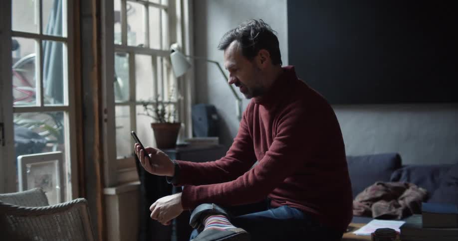 Man sitting over a coffee table at home talking on his smartphone