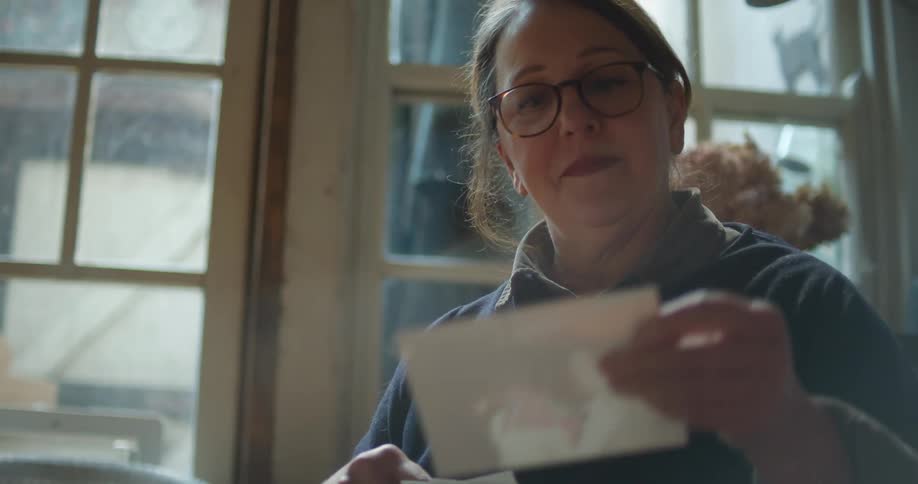A woman with glasses in a room looking at a photo with a window in the background