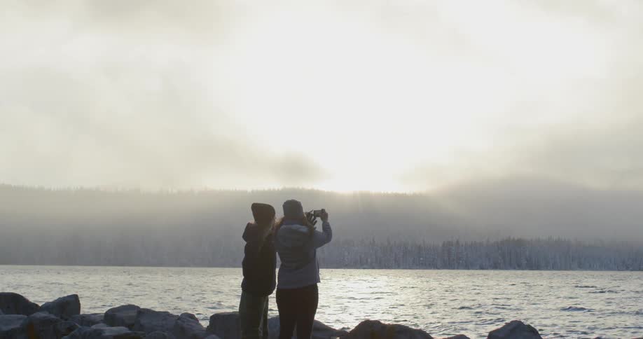 Two people stand by the water one takes a photo