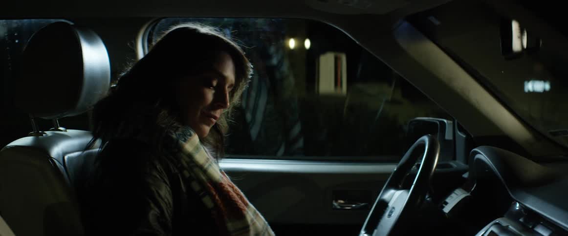 A woman checks her smartphone after getting into her car at night