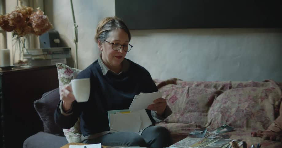 A woman with glasses in a room looking at photos with a wall and window in the background