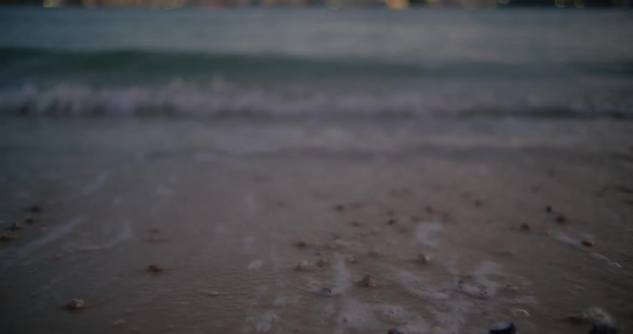 Ocean waves move pebbles and shells on the beach sand