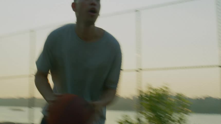 Two men play basketball on a city court at dusk