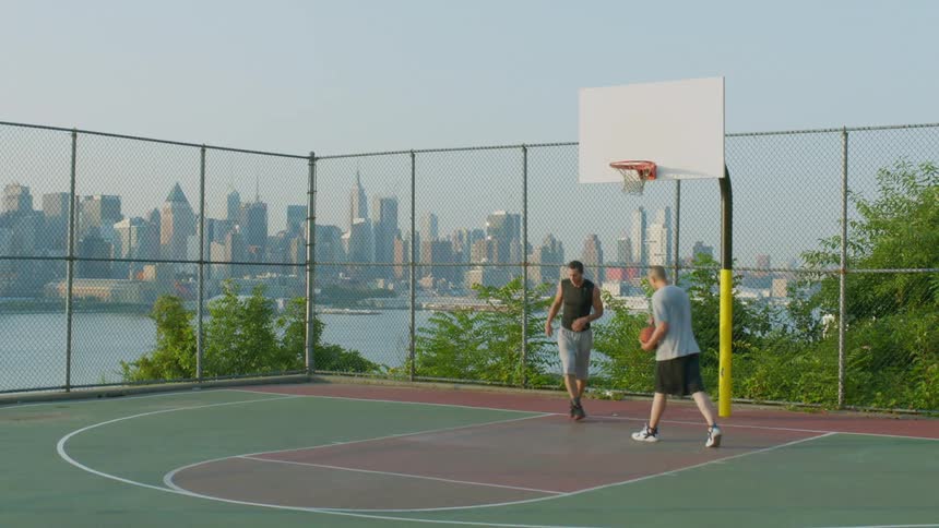 Two men playing basketball with a city in the background