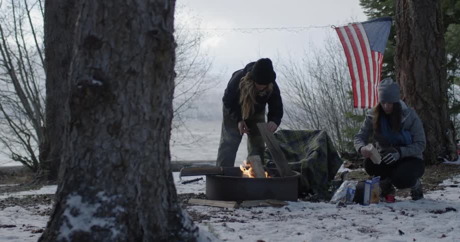 A woman puts wood in a campfire