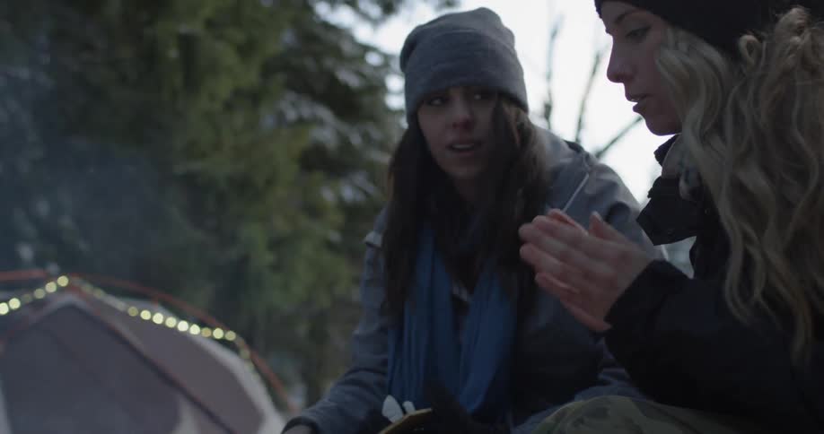 Two women warm up over the campfire in winter