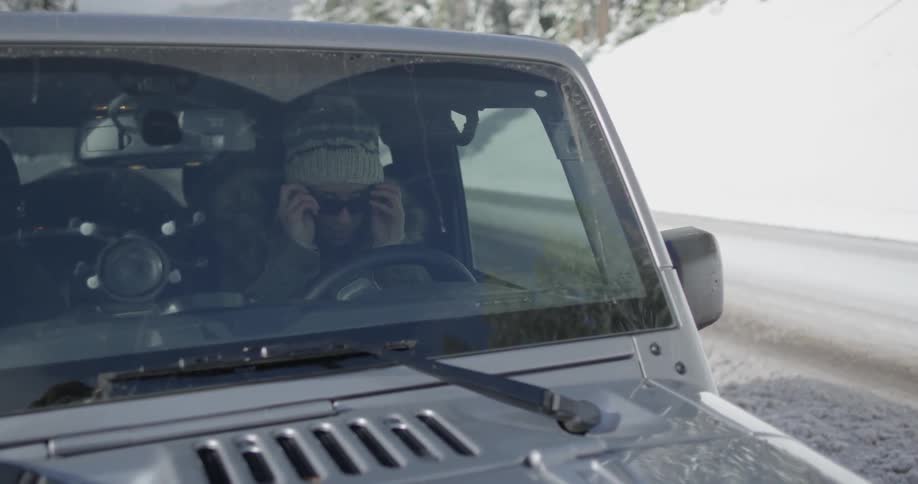 A woman puts on sunglasses while sitting behind the wheel of a car