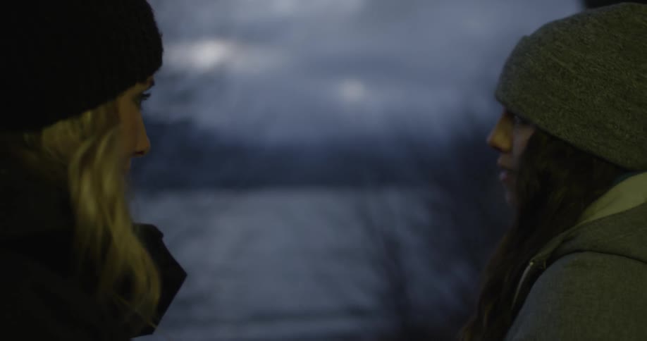 Two women standing near a lake talk and laugh on a cold winter night