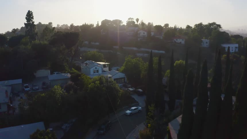 The sun rising over a neighborhood with large trees and hills