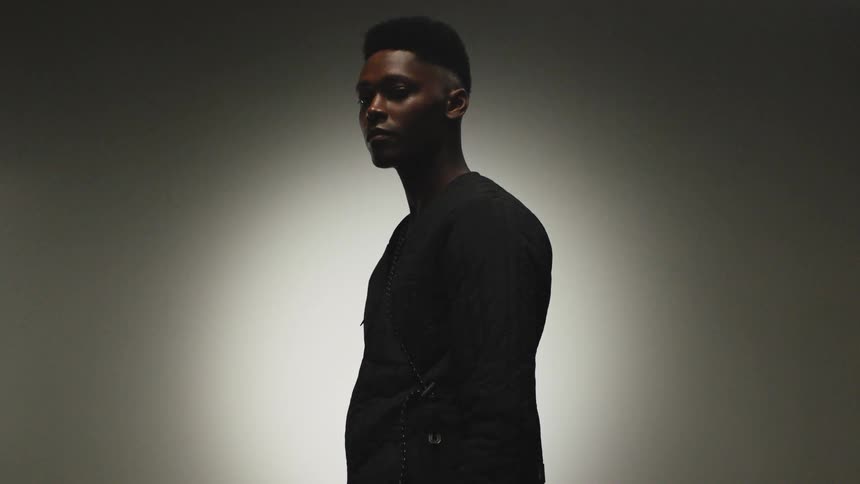 A man is standing next to a wall and is wearing a black shirt