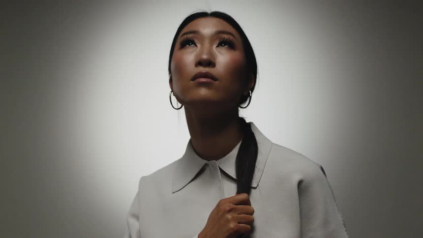 A woman with earrings standing and staring in a room with a wall in the background