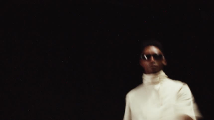 Man wearing shades moves and dances against black background