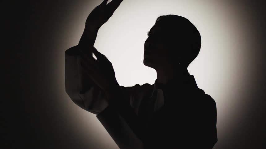 The silhouette of a woman as she holds her hands in front of her face and looks at them