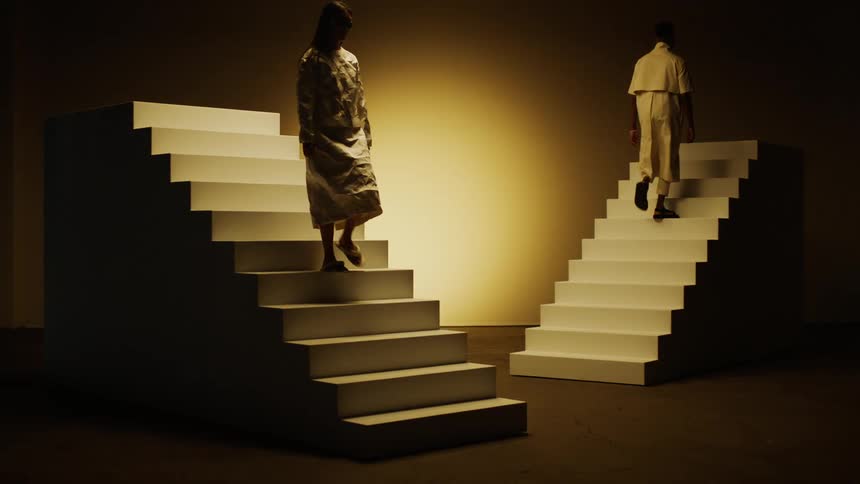Two people slowly walk up and down stairs on a stage