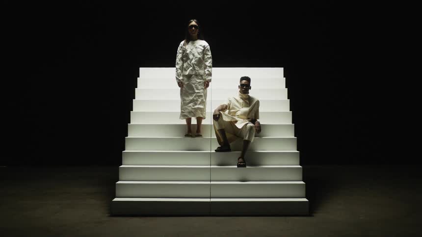 A man and woman wearing unique fashion pose for a photo shoot on a free standing staircase