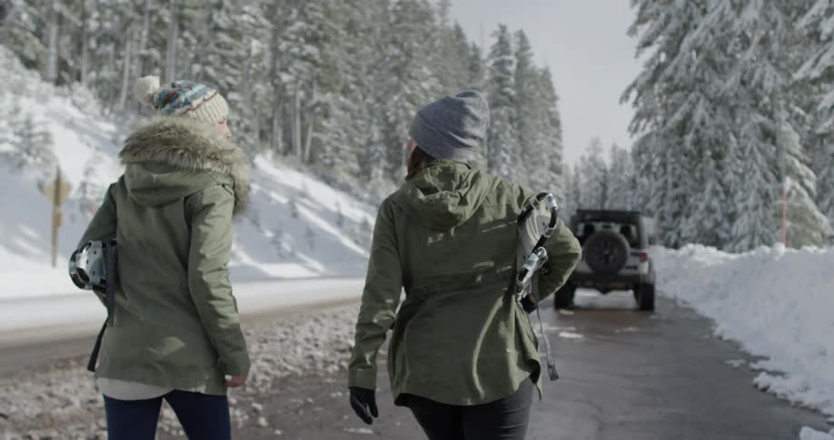 Two women walk down a road in a snow-covered forest