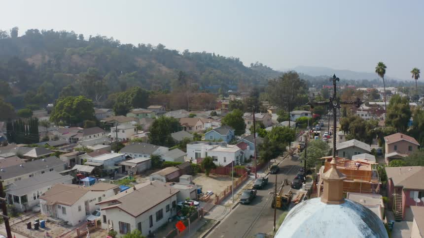 A neighborhood with a church houses and vehicles with trees the sky and clouds in the background