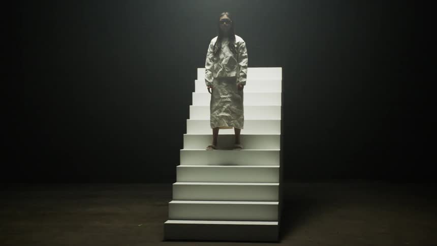 A model in a white dress poses on an unattached rotating staircase