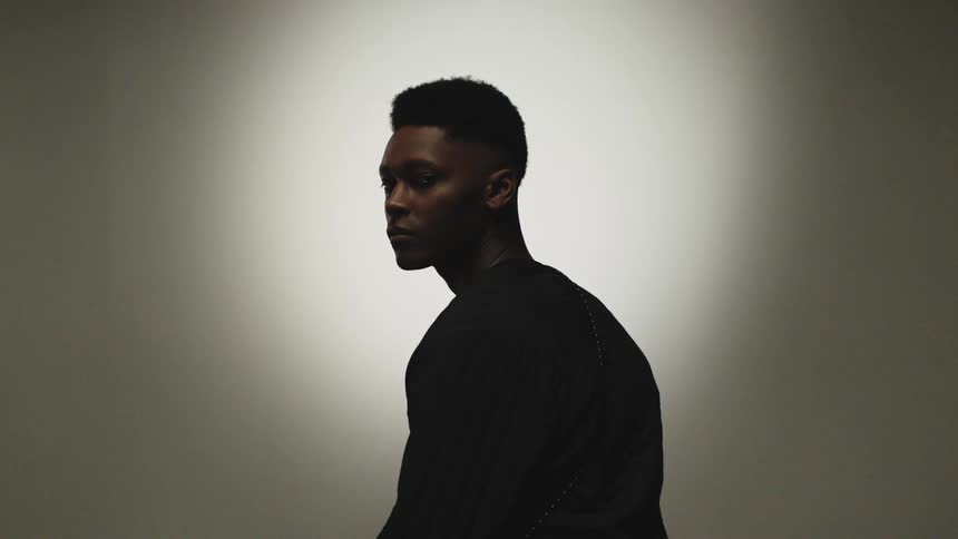A young black man in a sweater gazes over his shoulder into the camera